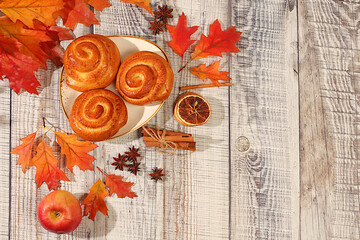 Cinnamon buns on wooden table with autumn fallen leaves, star anise, ginger and cinnamon, banner or display template, autumn greeting concept, menu mockup and advertisement for bakery.