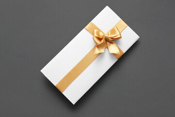 Paper card with bow made of golden ribbons on grey background