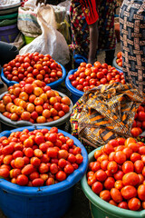 Vibrant red tomatoes in blue basins at a bustling African outdoor food market