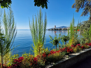 Sunny view of the Montreux promenade along Lake Geneva in Switzerland. Colorful flowerbeds, calm blue water, and a peaceful atmosphere capture the charm of this famous lakeside resort town.