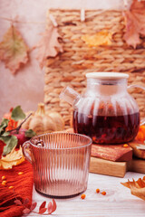 Vertical shot of a warm glass teapot filled with autumn fruit tea, an empty cup, pumpkins and seasonal leaves on a cozy Thanksgiving background.