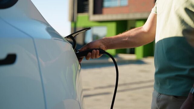Man unplugging charging cable from white electric car