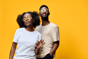 Fototapeta premium Stylish African American couple posing playfully in trendy outfits against a vibrant yellow background, showcasing confidence and happiness