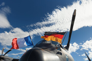 Military airplane and aircraft with two wavy national flags of Germany and France. German and French air force. Alliance of European allies and armed forces and defense. Blue sky as copy space