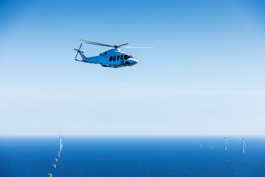 Large helicopter flying over the Baltic Sea with landscape and wind farms in the background.