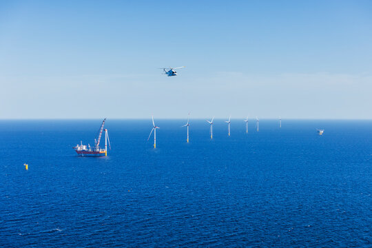 Large helicopter flying over the Baltic Sea with landscape and wind farms in the background.
