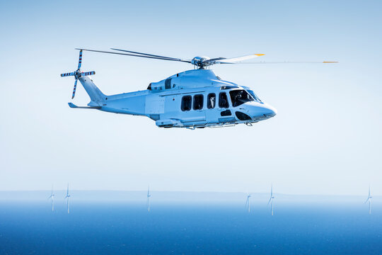Large helicopter flying over the Baltic Sea with landscape and wind farms in the background.