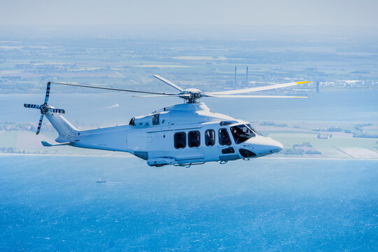 Large helicopter flying over the Baltic Sea with landscape and wind farms in the background.