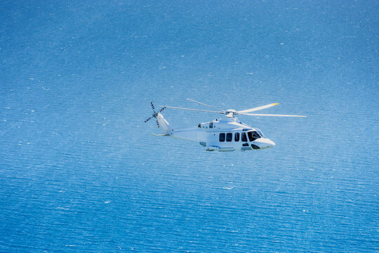 Large helicopter flying over the Baltic Sea with landscape and wind farms in the background.
