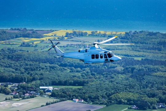 Large helicopter flying over the Baltic Sea with landscape and wind farms in the background.
