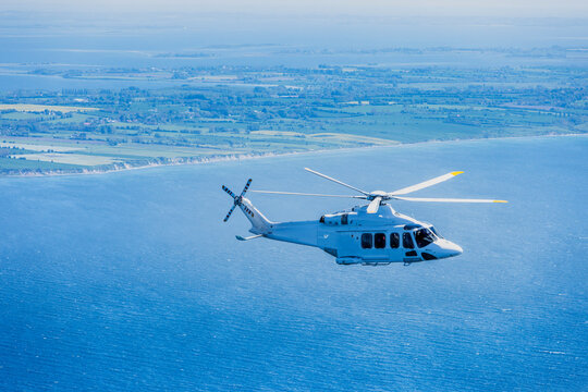 Large helicopter flying over the Baltic Sea with landscape and wind farms in the background.