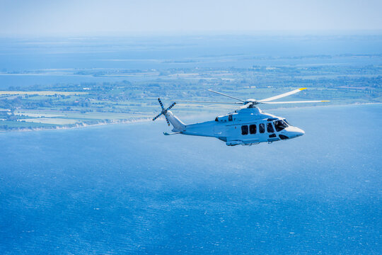 Large helicopter flying over the Baltic Sea with landscape and wind farms in the background.