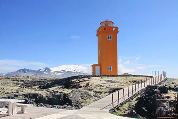 orange lighthouse with snow-capped mountains in the background