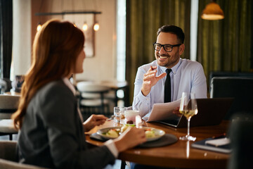 Happy businessman talking to his colleague while analyzing reports during lunch in restaurant.