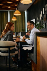 Happy business coworkers communicating while eating in restaurant.
