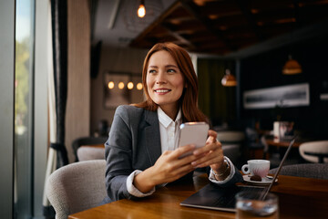 Happy businesswoman using smart phone while working on laptop in cafe,