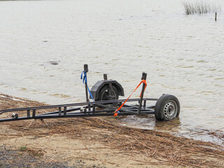 A boat trailer is sitting in the water, with a rope tied to it. The water is murky and the boat trailer is partially submerged. Fishing and aqua sport concept.