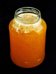 Glass jar of golden bee honey is on a dark background. Fine organic product concept. Agriculture and food industry.
