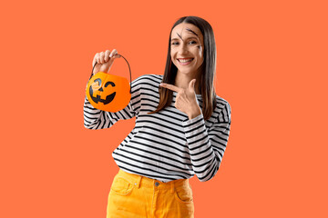 Beautiful young happy woman pointing at Halloween pumpkin basket on orange background