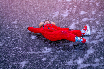 A girl in a red tracksuit lies on the ice of a frozen lake. Child's fall while skating