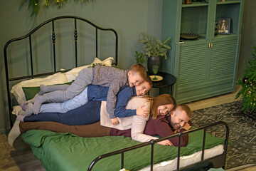 Parents and sons are lying next to each other on a bedroom bed decorated for New Year and Christmas. Happy happy family on the weekend
