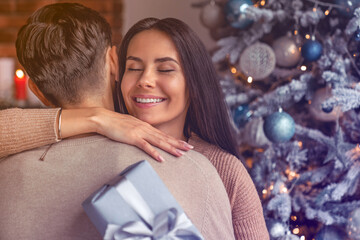 Happy couple celebrating Christmas together with gift. Husband spouse boyfriend giving sharing a...