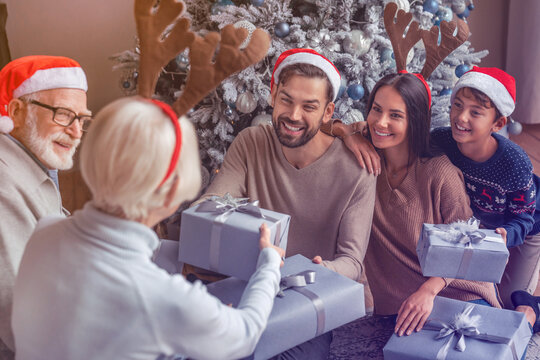 Mature woman giving New Year gift to her adult son while family celebrating at living room. Present gift sharing giving for Christmas holiday in winter