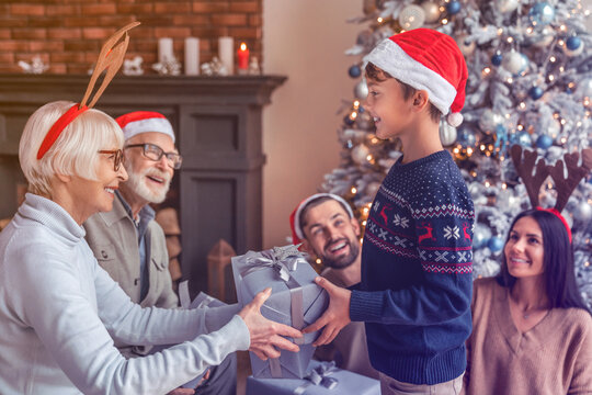 Happy three generation family celebrating Christmas New Year together giving sharing gifts presents in the living room together at home. Winter holiday season