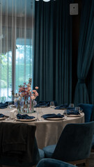 wedding decoration of a round table with a floral arrangement in blue and pink colors. Rose, delphinium, carnation, dahlia, eryngium, candles, blue napkins