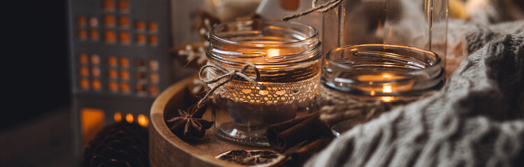 Banner. Cozy home holiday atmosphere. Idea for handmade christmas decorations: aromatic candles in glass jars. Cinnamon sticks, anise, dry citrus, homemade gingerbread cookies. Fairy lights