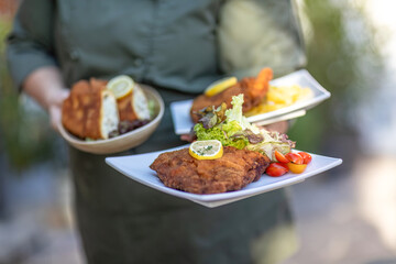 Waiter serving vegetarian and classic cordon bleu with potato salad and lemon garnish at an outdoor restaurant