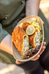 Waiter serving vegetarian and classic cordon bleu with potato salad and lemon garnish at an outdoor restaurant