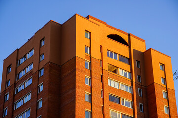 Modern orange brick apartment building under clear blue sky at sunset in a city neighborhood