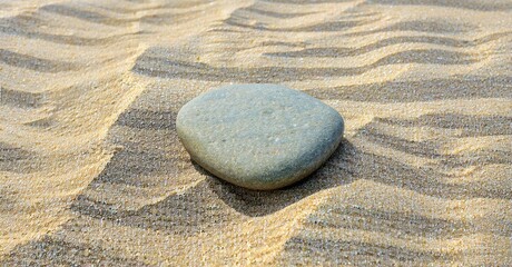 Obraz premium Smooth stone rests upon rippled sand. Warm tones dominate scene, creating peaceful texture. Simple composition, natural light.