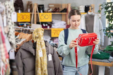 Glad adolescent female customer reviewing colorful handbags during Black Friday shopping