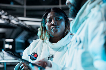 Female astronaut scientist looking at orbital navigation data on tablet, recording findings. Woman researcher wearing cosmonaut gear in spaceship doing research, reviewing onboard analytics