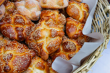 Traditional Mexican Pan de Muerto (Bread of the Dead) with sesame seeds, stacked in a rustic basket. Delicious iconic Day of the Dead food.
