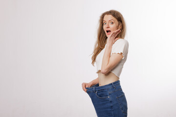 Surprised woman showing oversized jeans after weight loss success in studio