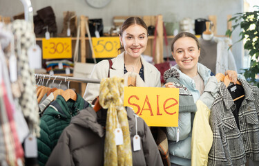 Fototapeta premium Happy family holding sign saying Sale for Black Friday sale of winter clothing collection standing in interior of modern clothing boutique