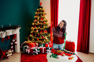 Woman preparing Christmas decorations in festive home interior with decorated tree, presents, and...