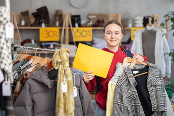 Teenage girl choosing outerwear and holding yellow sign in clothing store