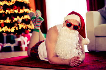 Funny Santa Claus relaxing at home with Christmas tree and playful decorations in a stylish...