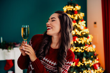 Joyful woman enjoying the festive atmosphere indoors by a sparkling Christmas tree during the...