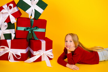 playful christmas gifts stacked high beside a smiling young girl resting on a bright yellow...