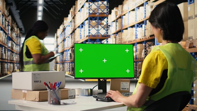Asian staff looking at isolated screen shipping route on package tracking software, updating the delivery details on airway bills. Works in warehouse with green screen on computer. Camera A.