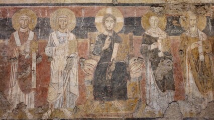 Rome, Italy - 13 January 2025. In Santa Maria Antiqua, a worn fresco depicts Christ between four saints, all with halos and gospel books, set against a red and black background. © Michael