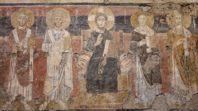 Rome, Italy - 13 January 2025. In Santa Maria Antiqua, a worn fresco depicts Christ between four saints, all with halos and gospel books, set against a red and black background.