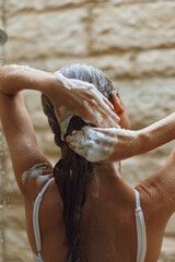 Woman washing hair with shampoo foam in shower, wet skin, natural light, spa-like atmosphere, clean...