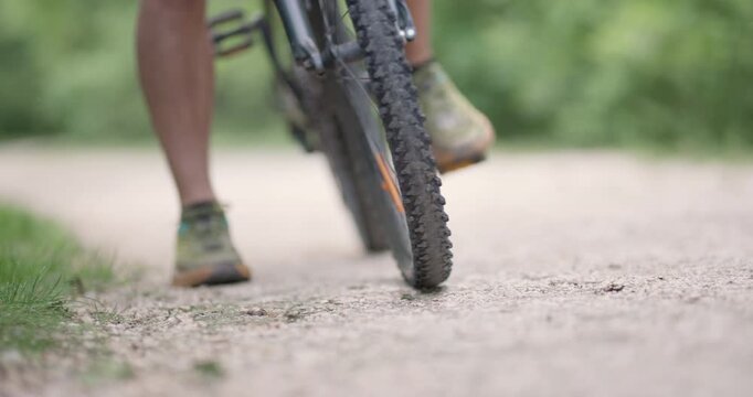 Abstract mountainbiker putting leg on the ground. Man riding a mountainbike on a dusty dirth road path. Closeup pedal shoe and gear shift. Recorded at 120 fps on cinema camera.