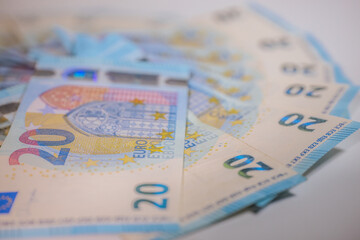 Close-up of multiple €20 euro banknotes arranged in a fanned-out pattern on a white surface, highlighting the detailed security features and design elements.